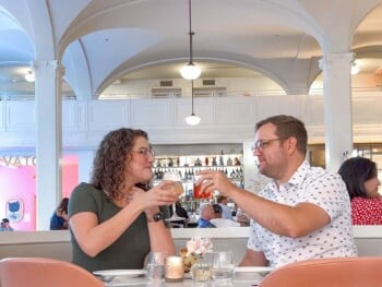 Luke and Meagan toasting their cocktails in the brightly lit Lobby Bar at Quirk Hotel